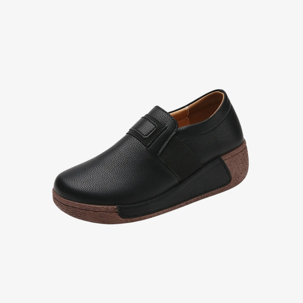 Mocassins compensés pour femme en similicuir noir, au design ergonomique pour un confort optimal. Ces chaussures sont dotées d'une semelle marron épaisse et texturée, offrant un excellent maintien. Leur style épuré avec une fermeture élastique facilite l'enfilage tout en restant élégant et pratique.