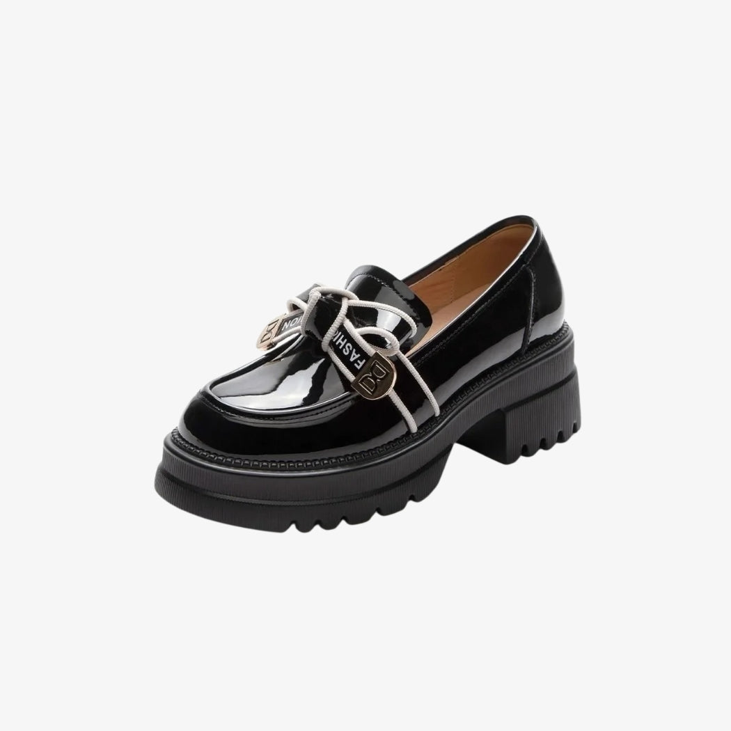 Mocassins pour femme en cuir noir brillant, dotés de talons épais crantés pour un style moderne et audacieux. Une décoration avec des lacets blancs et des ornements métalliques dorés sur le dessus ajoute une touche élégante et originale à ces chaussures chic et confortables.