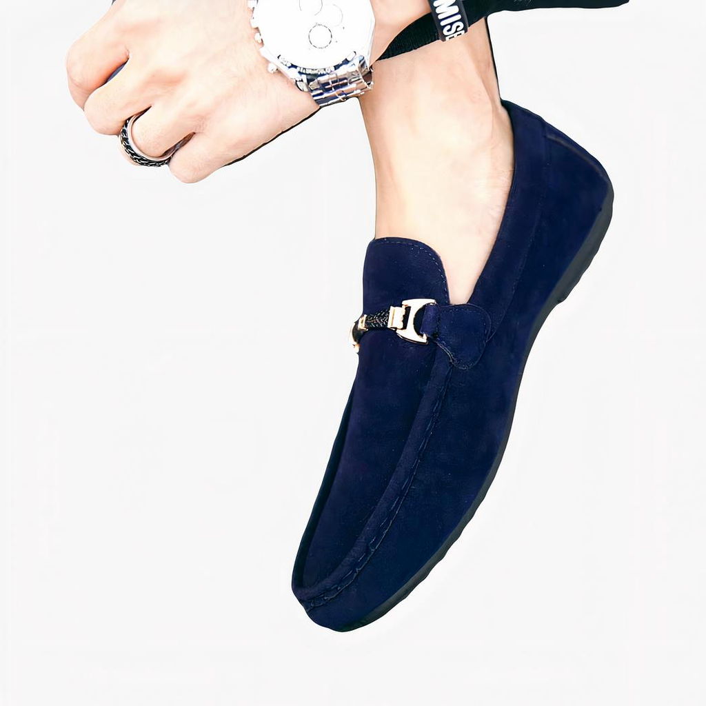 Pieds d'une personne portant des mocassins bleus avec une boucle dorée sur le devant et portant une montre au poignet