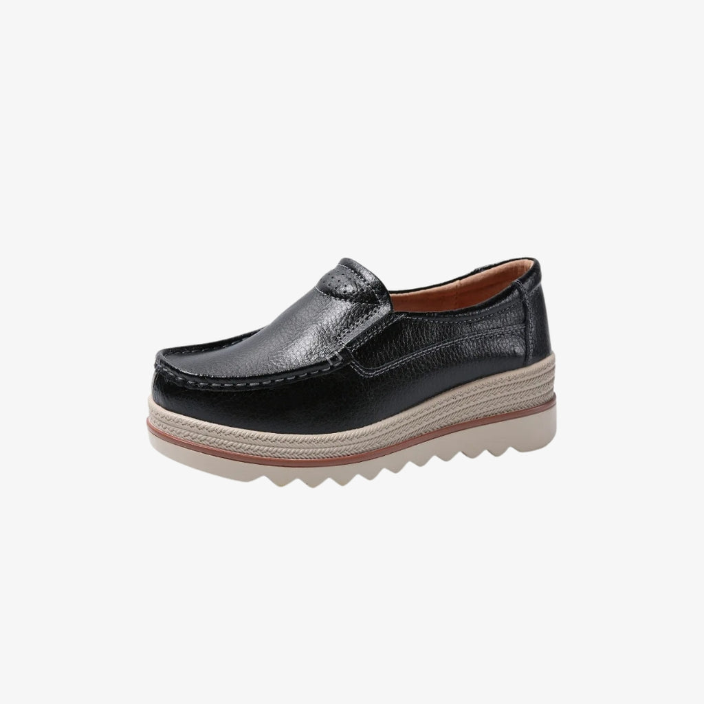 Mocassins compensés pour femme en cuir noir, au design élégant et intemporel. Ces chaussures présentent une semelle épaisse beige avec des détails tressés et une base crantée pour une meilleure adhérence. L'intérieur est conçu pour offrir un confort optimal tout au long de la journée.