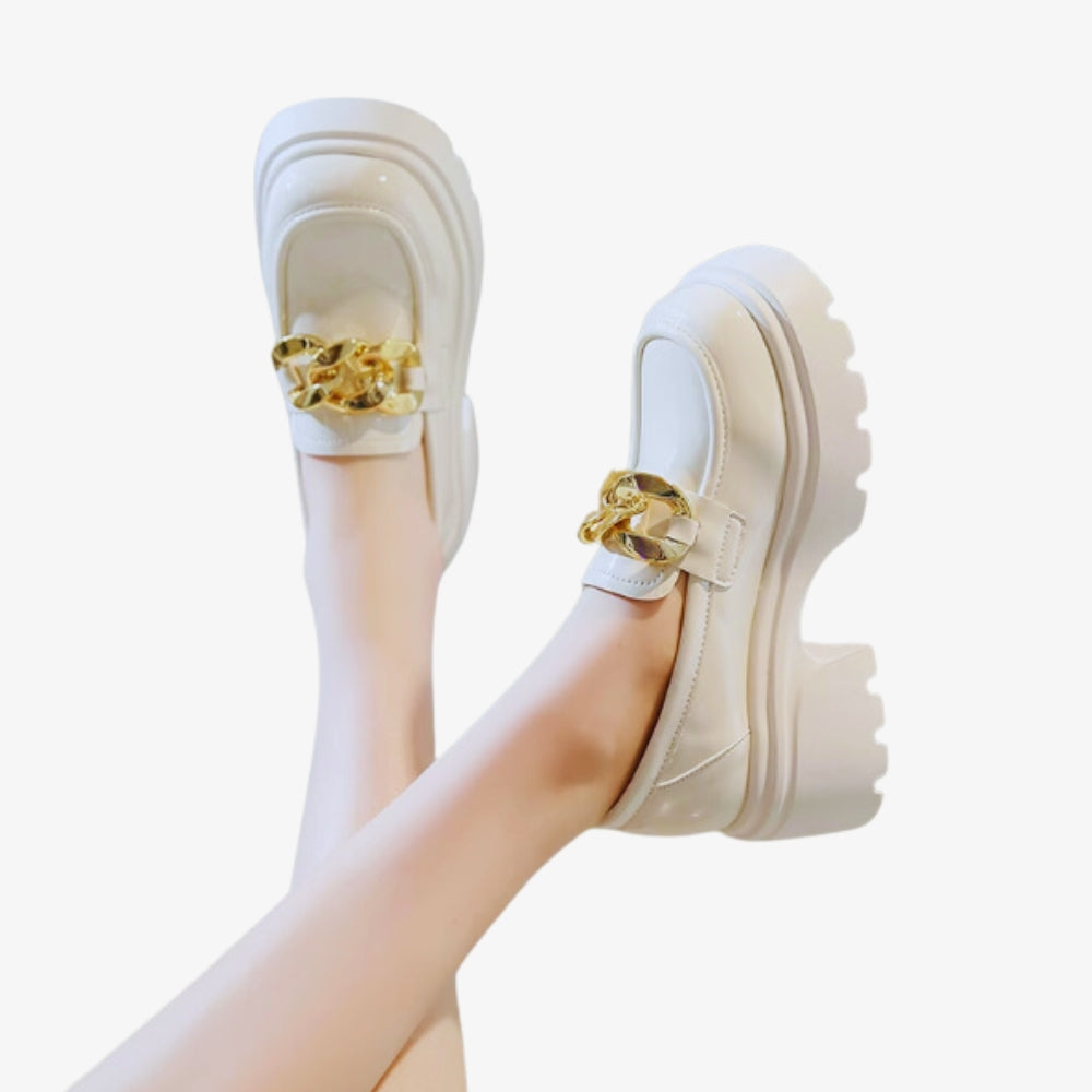 Mocassin blanc avec une grosse semelle noire épaisse et des boucles en or sur fond blanc