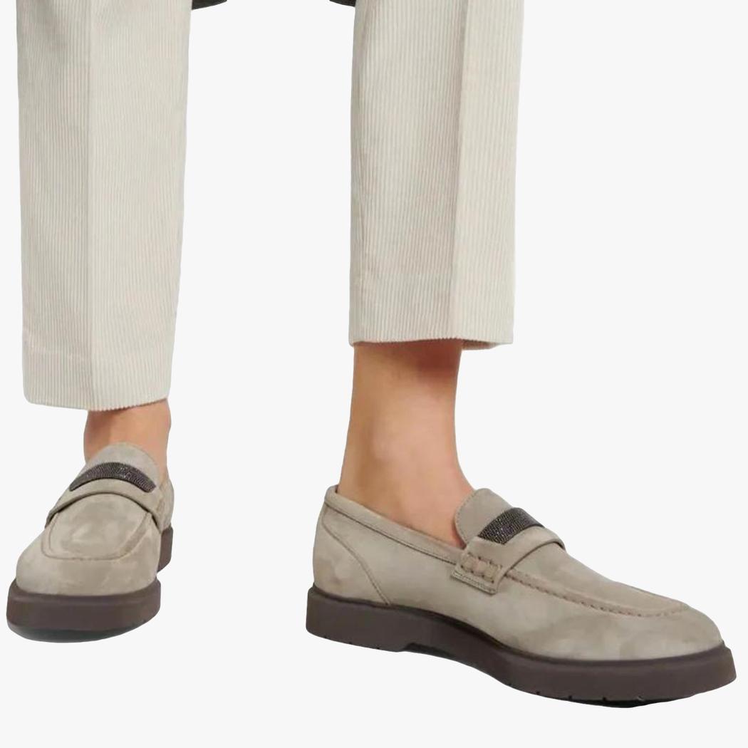 on voit les pieds d'une femme qui porte un pantalon de tailleur beige et des mocassins gris en daim véritable pour femme