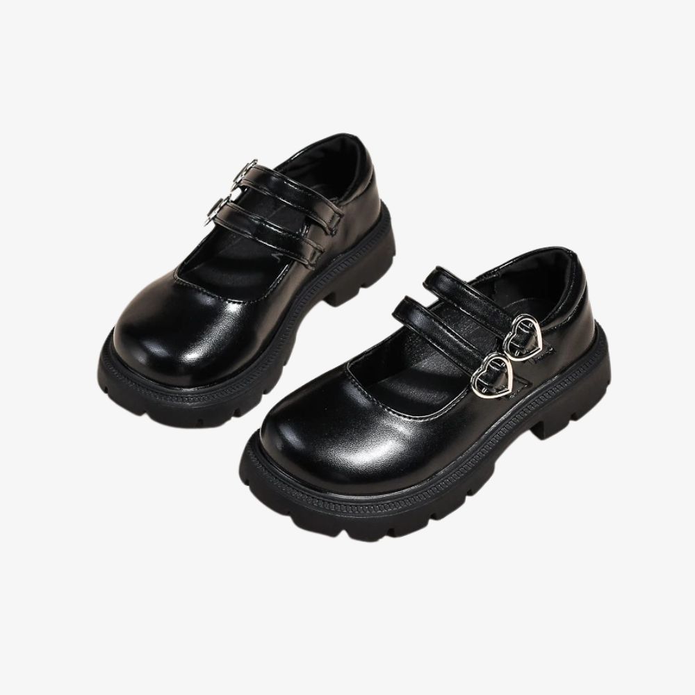 Paire de mocassins noirs avec double bride et un détail coeur dessus, sur fond gris.