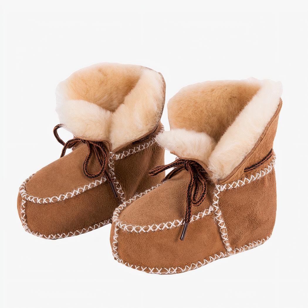 De profil, paire de bottines de mocassins indiens en croute de cuir camel avec surpiqures blanches et fourrure beige apparente à l'intérieur. Il y a des lacets marrons sur le dessus