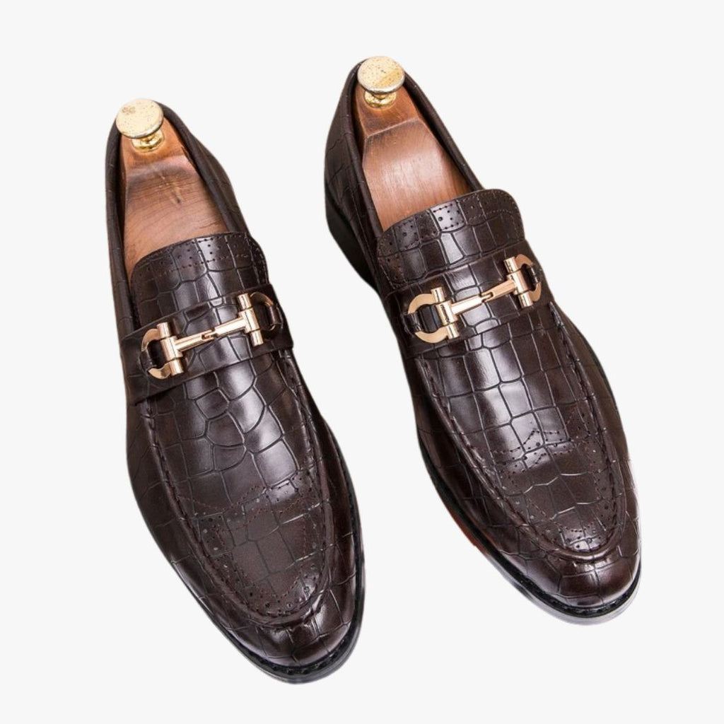 Mocassin en cuir végan effet croco et à boucle dorée en version marron et sur fond blanc cassé.