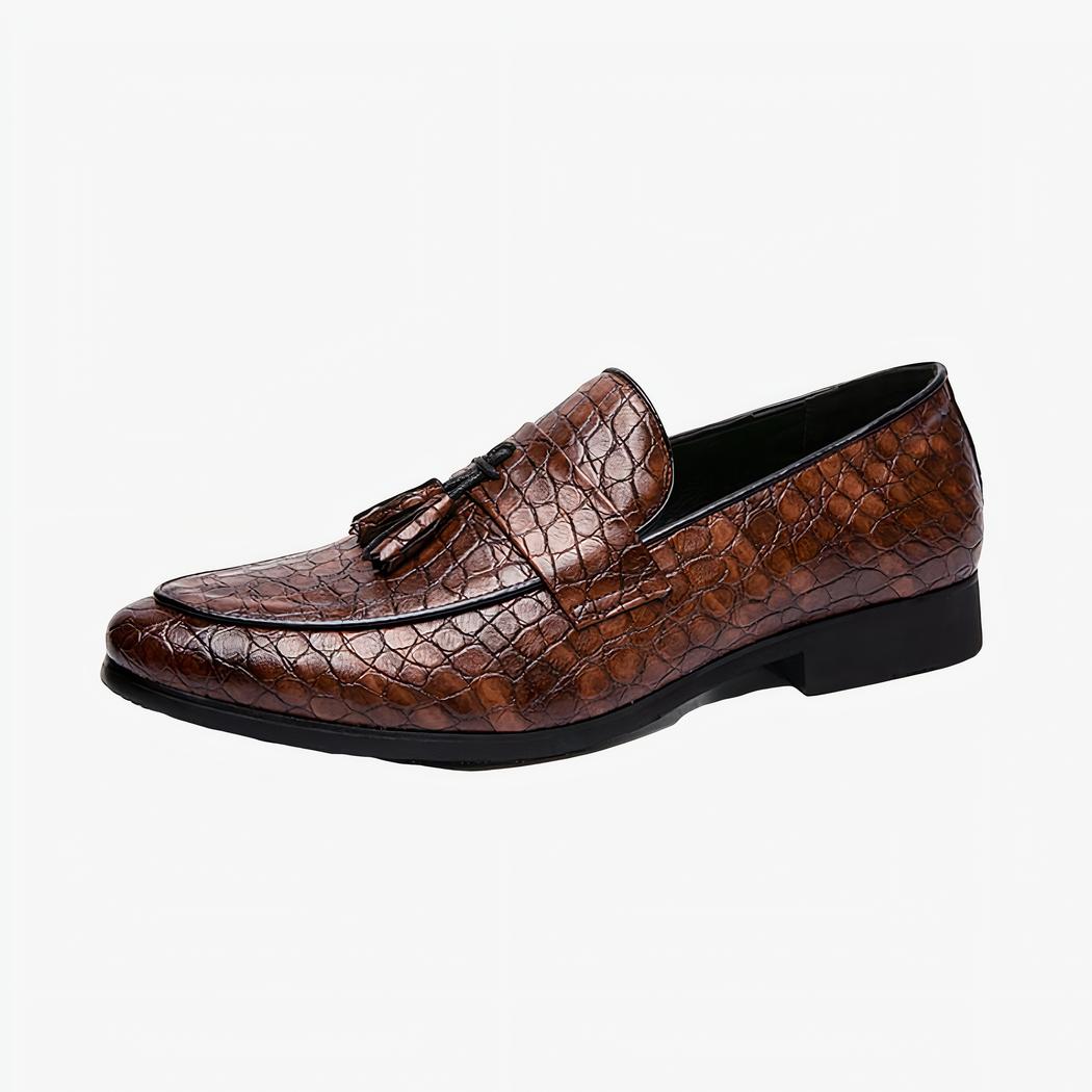 Un mocassin en cuir marron façon serpent avec une bande sur le dessus et des glands décoratifs, sur un fond blanc.