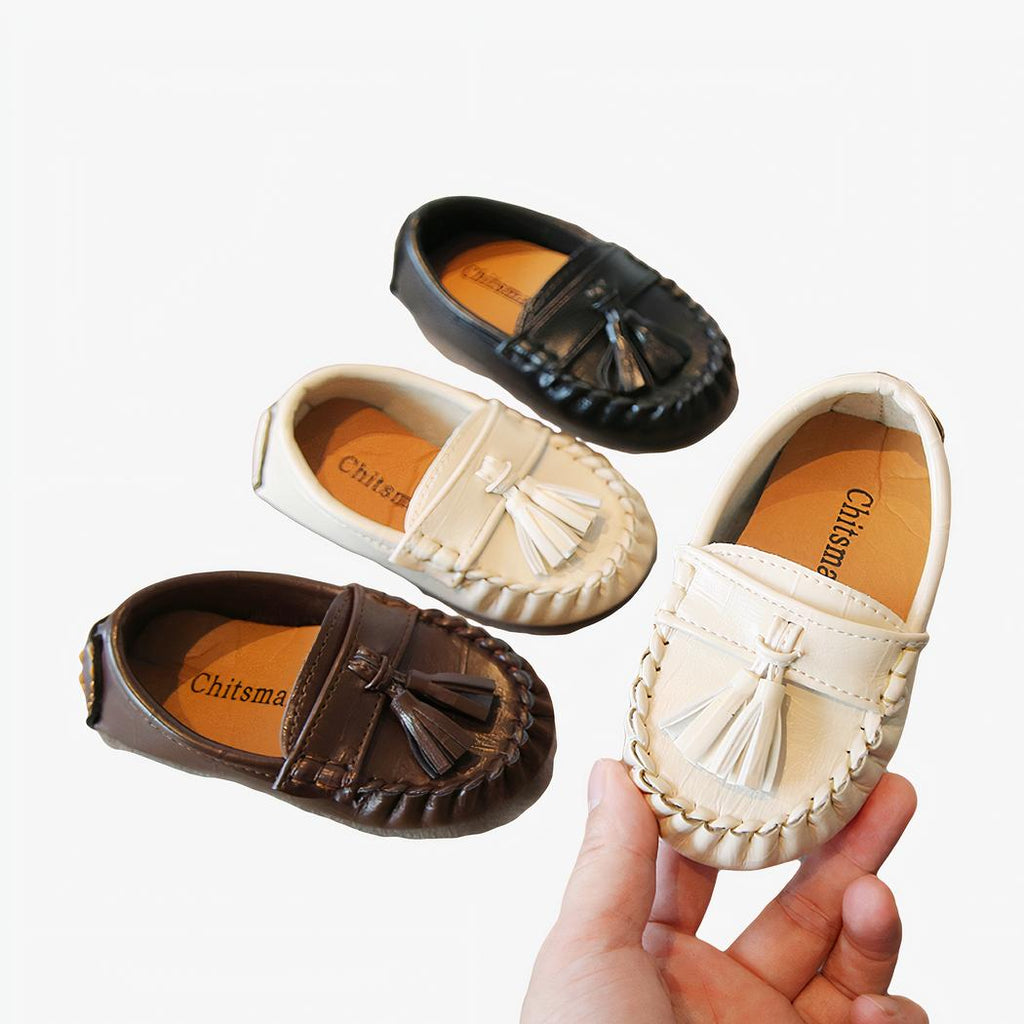 Plusieurs petits mocassins à gland pour enfant sur une table et un tenu dans une main.