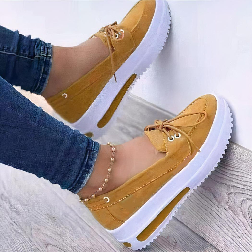 Photo d'une paire de mocassins à plateforme jaune portée par une femme en jean, sur un sol en parquet et un mur blanc