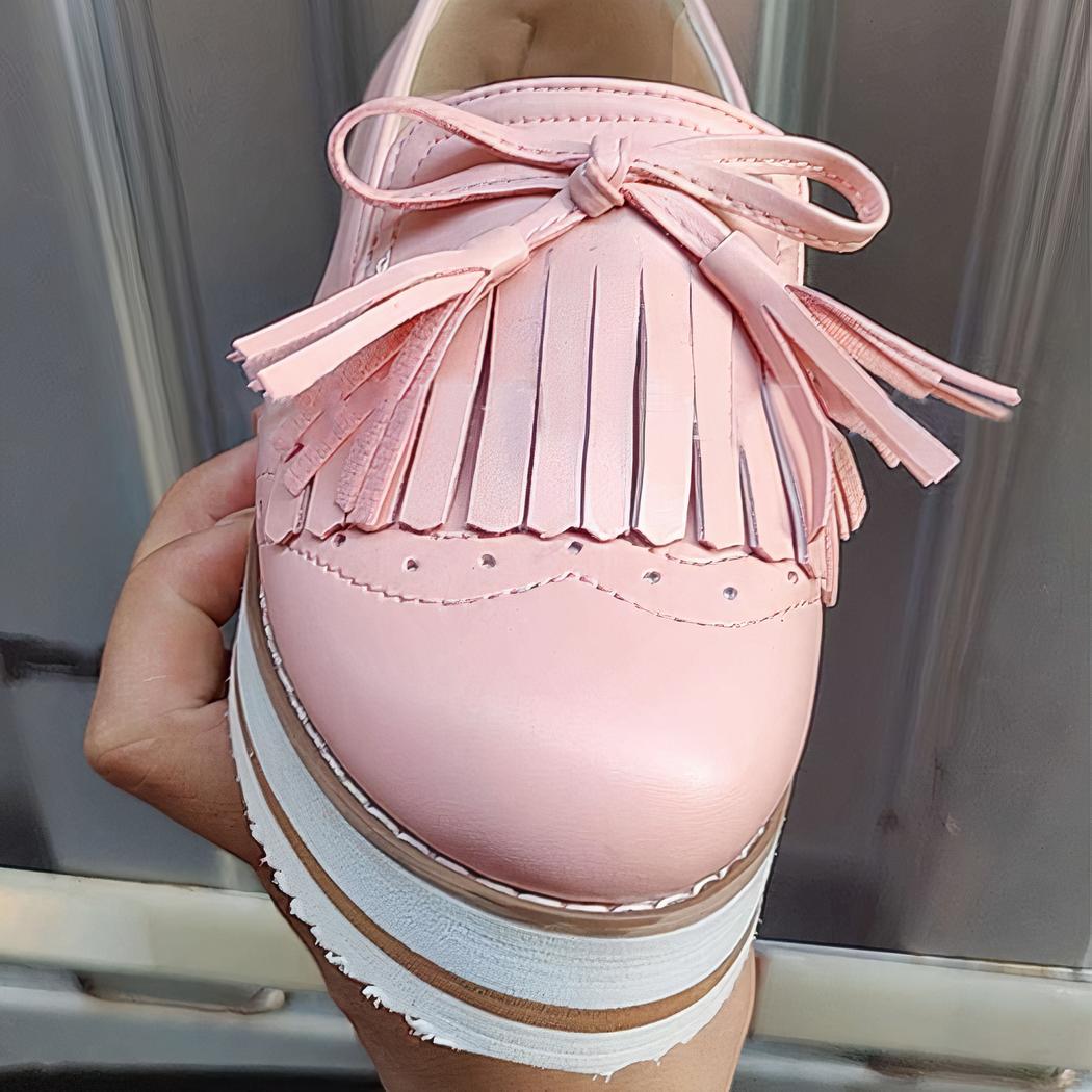 Photo d'un mocassin rose compensé à franges porté devant une porte