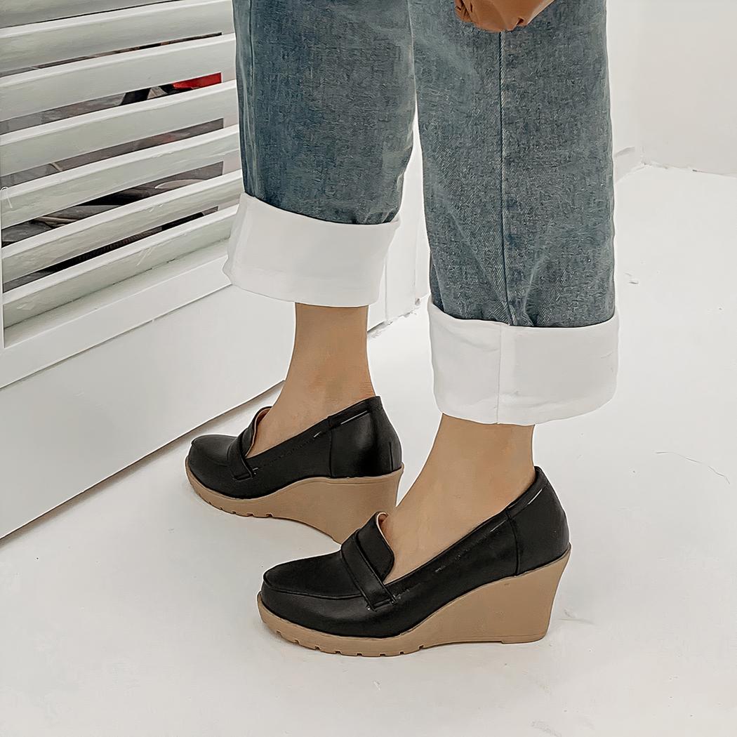 Photo d'une paire de mocassins compensée noire portée par une femme en jean sur un sol gris