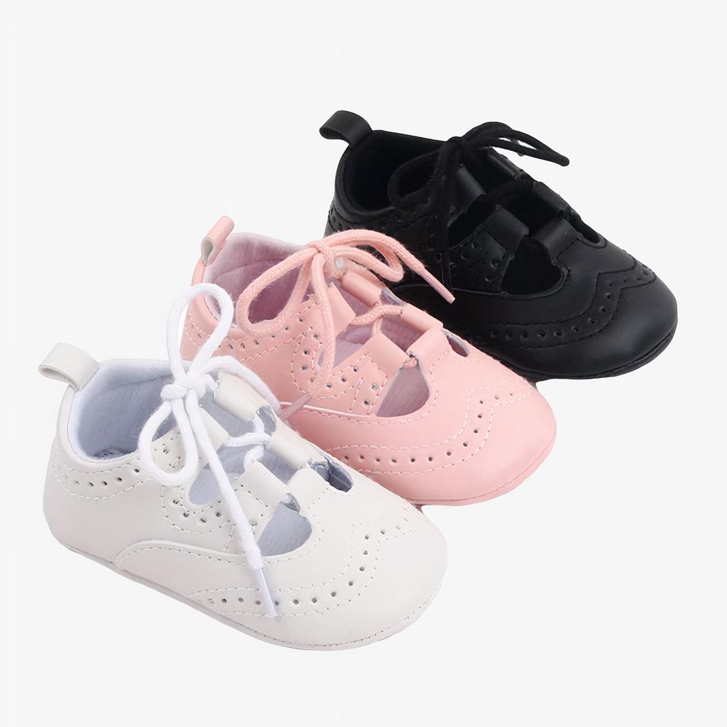Trois mocassins à lacets pour bébé alignés en diagonale, de couleur blanche, rose et noire