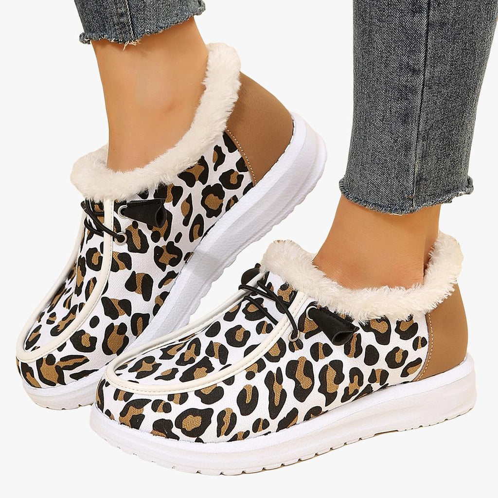 Porté avec un jean bleu, une paire de mocassins d'hiver blancs avec imprimé léopard et bordure en fourrure beige apparente. La semelle est blanche et épaisse et il y a des lacets noirs décoratifs sur le dessus du chaussant