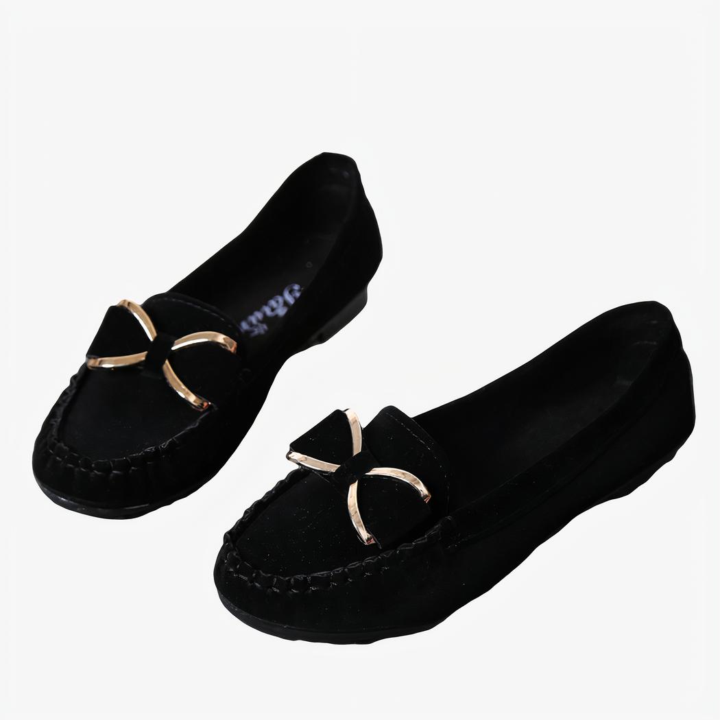 Paire de mocassins noirs avec un nœud doré posés au sol avec des accessoires autour