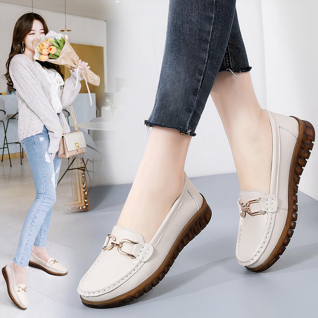 Photo d'une paire de mocassins blanc portée par une femme avec un jean noir, sur un sol gris et avec en fond une femme