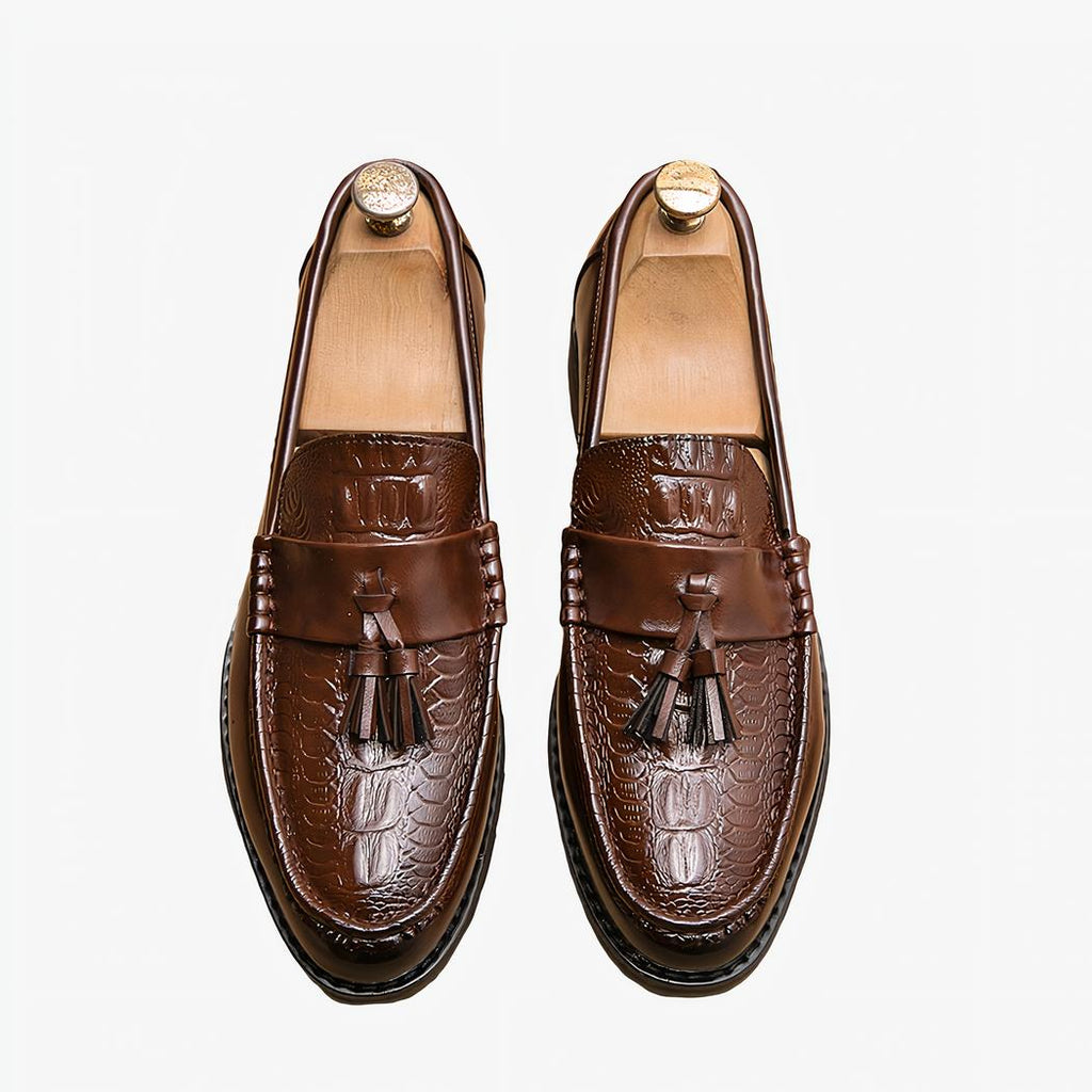 Mocassins marron à gland sur sol beige avec un chausse pied couleur or à coté