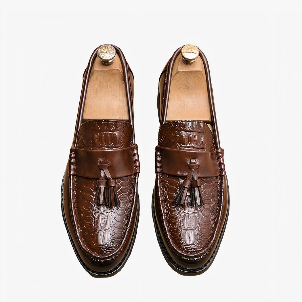 Mocassins marron à gland sur sol beige avec un chausse pied couleur or à coté