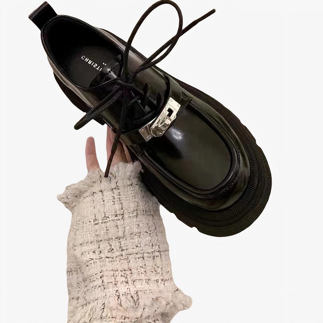 Main d'une femme tenant un mocassin noir à lacets, dans la pièce d'une maison