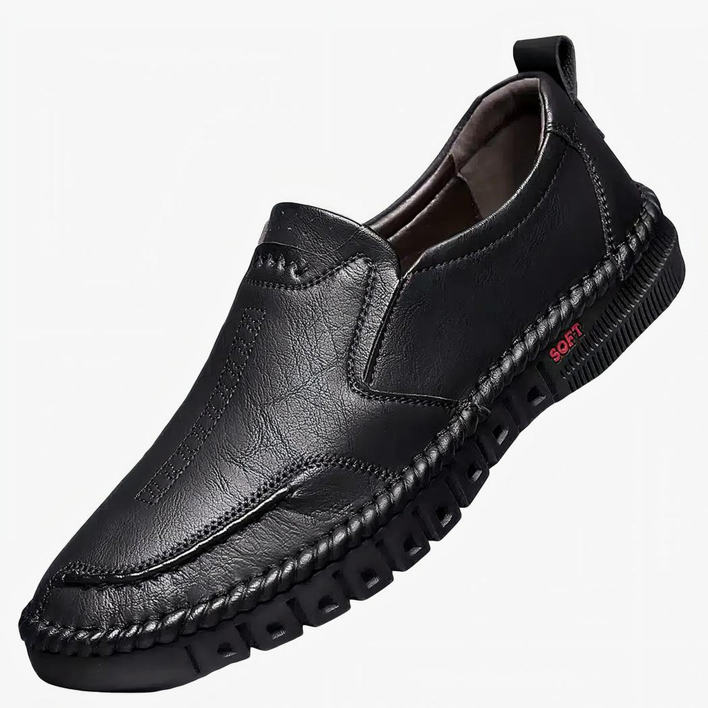 Mocassin noir posé sur un support blanc, fond gris.