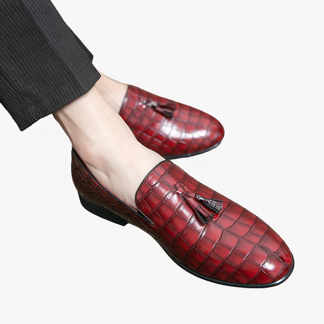 Pieds portant des mocassins rouges effet peau de crocodile et avec un gland sur le dessus de la chaussure