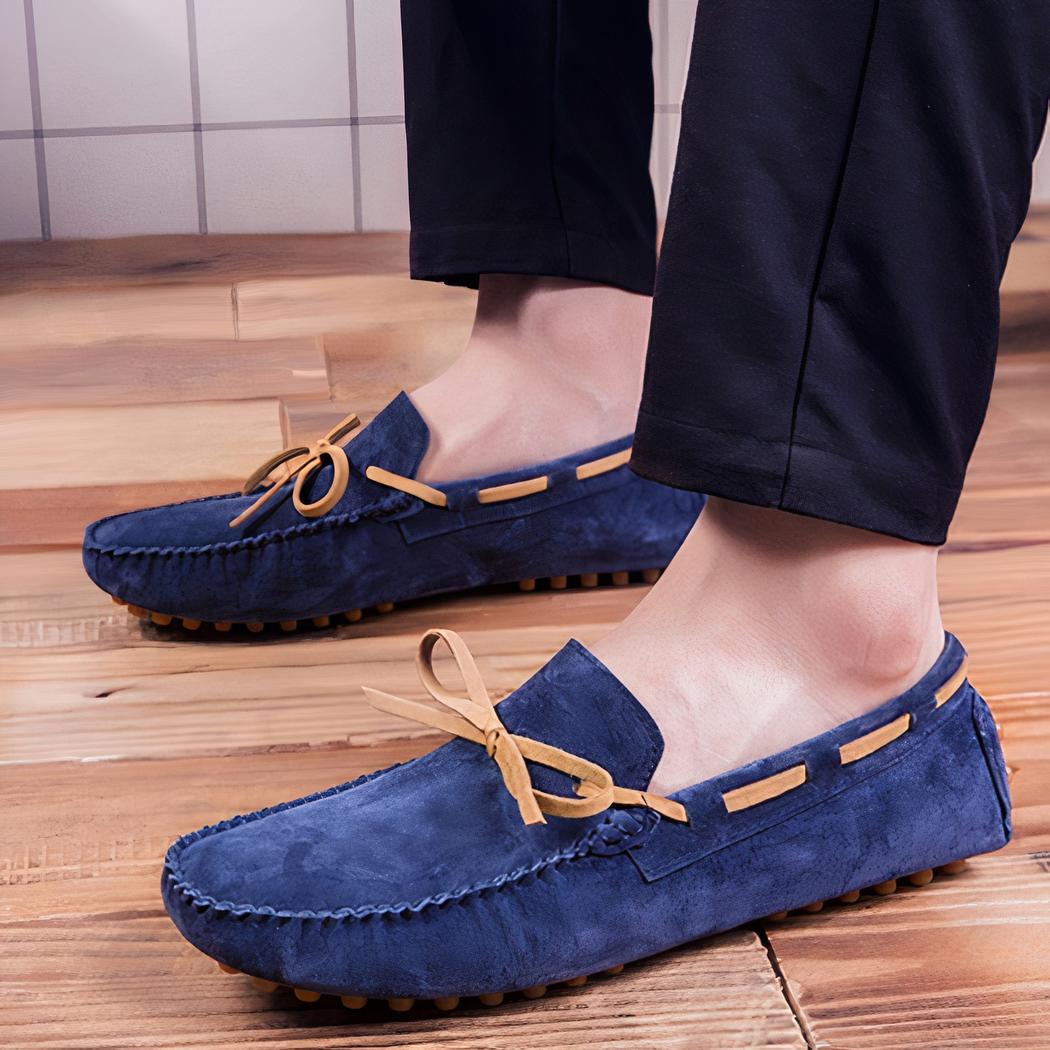 Paire de mocassins bleus tenus dans les mains d'une personne portant une montre et une chemise à rayures bleus et blanches