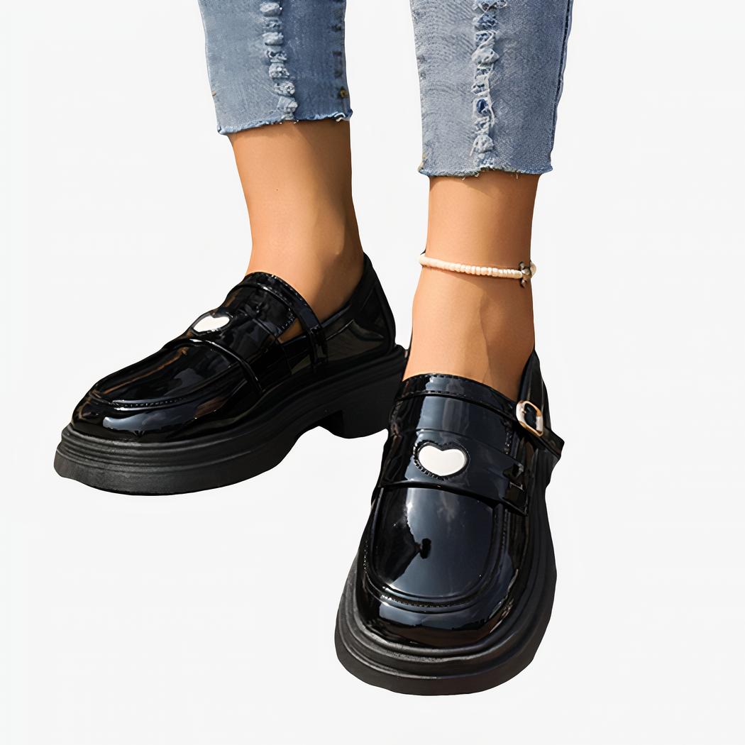 mocassins noirs en simili cuir verni, avec un coeur blanc sur le devant, porté par quelqu'un avec des jeans, debout sur des escaliers