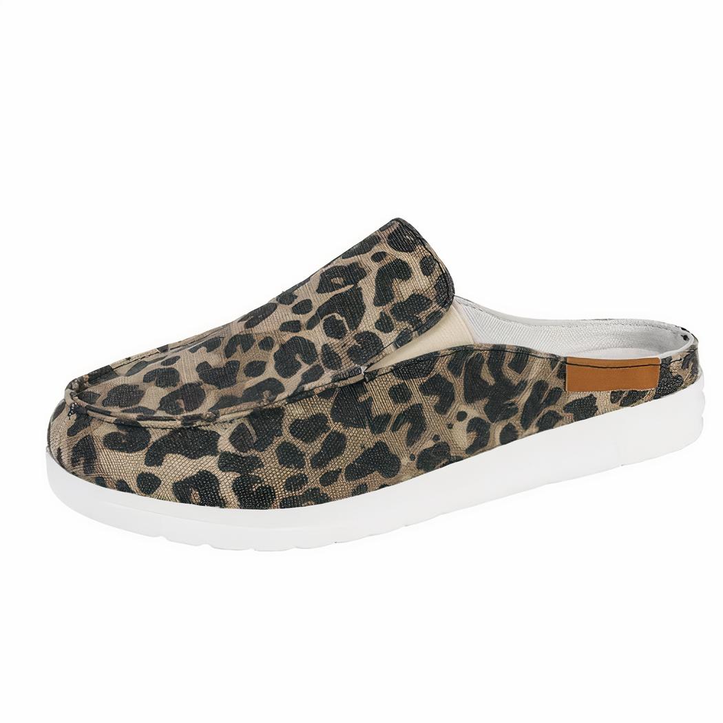 Présentée de profil, paire de mules mocassins sport ronds en toile imprimé léopard avec semelle blanche épaisse. Une chaussure sur un présentoir blanc et une en dessous sur un sol blanc