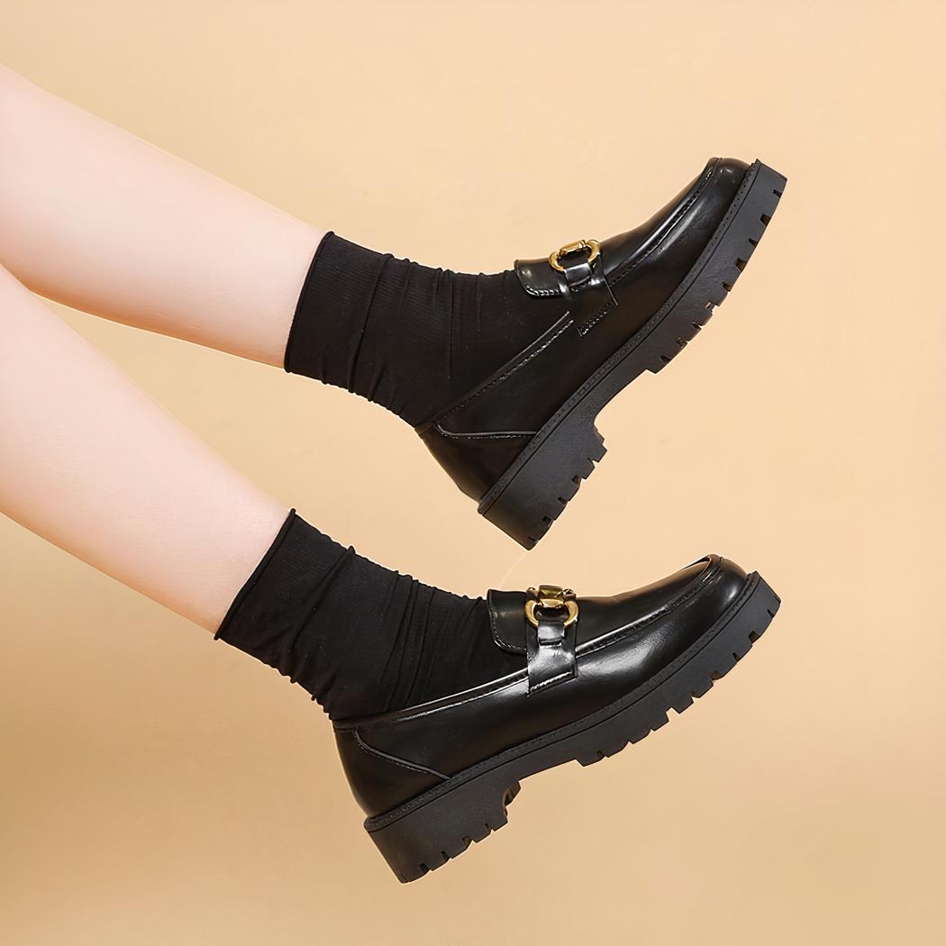 Photo d'une paire de mocassins à plateforme noire portée par une femme sur fond beige