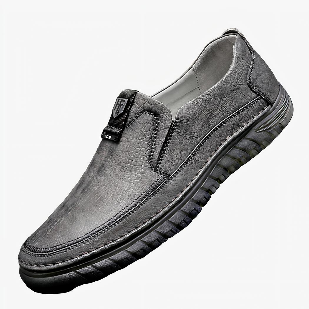 Mocassin orthopédique gris, posé en équilibre sur un élément blanc, sur un fond gris
