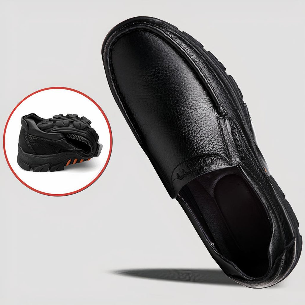 Photo d'une paire de mocassins orthopédiques en cuir noir à semelle épaisse, une chaussure est couchée sur le sol, l'autre est tenue dans une main.