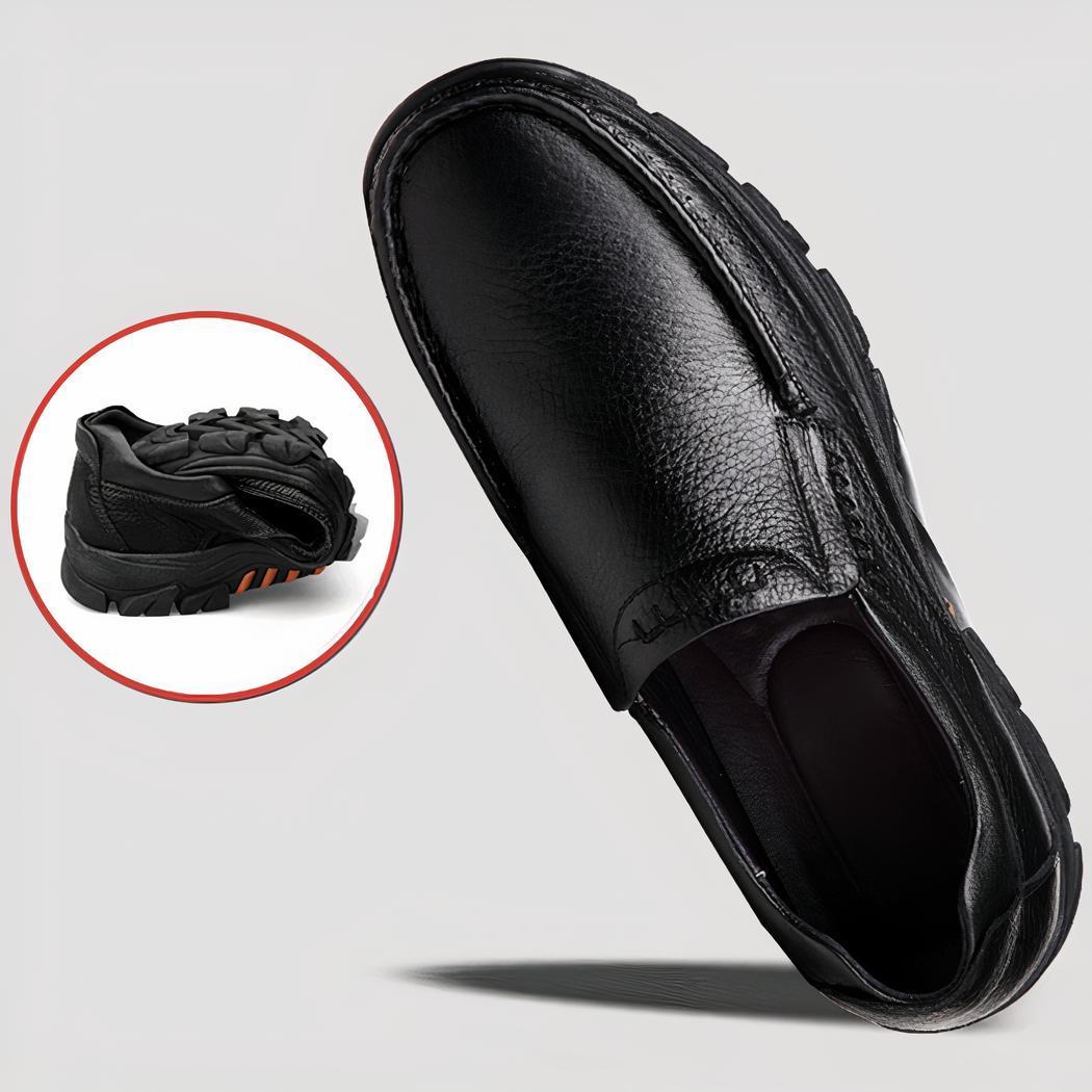 Photo d'une paire de mocassins orthopédiques en cuir noir à semelle épaisse, une chaussure est couchée sur le sol, l'autre est tenue dans une main.