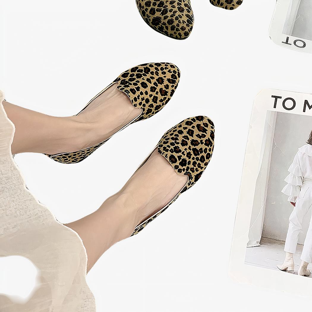 Paire de mocassins simple avec imprimé léopard vue du haut porté avec une jupe blanche et pieds nus. Le sol est en moquette beige et il y a un magazine blanc à côté