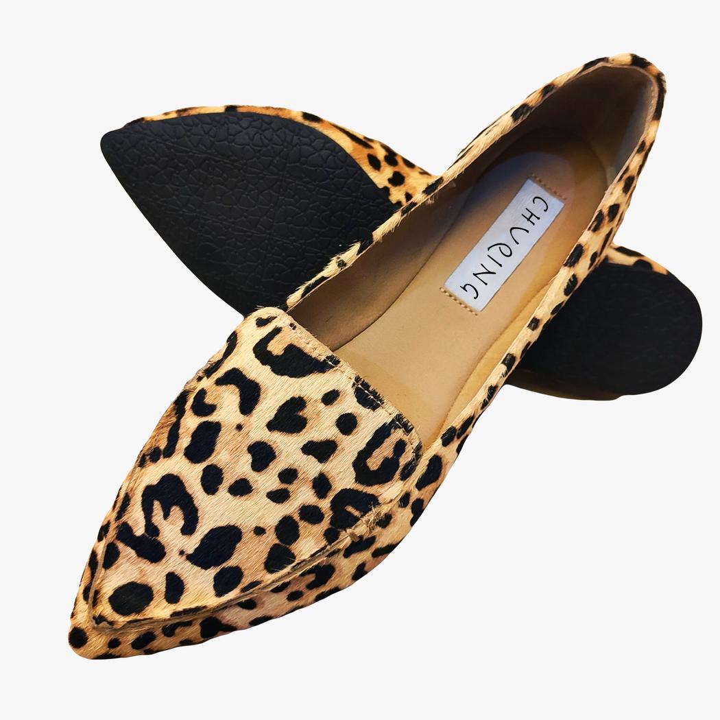 Sur fond rose marbré, une paire de mocassins pointu en daim et imprimé léopard marron.