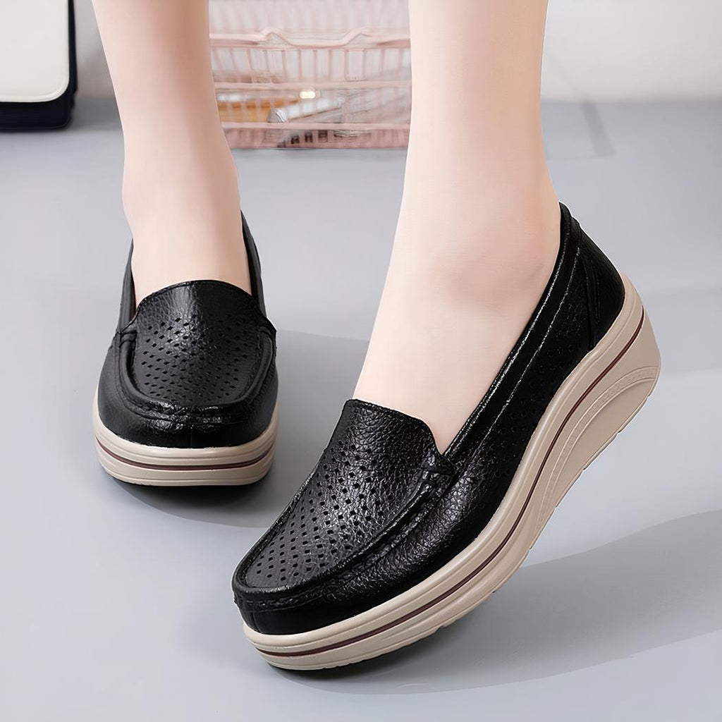 Photo d'une paire de mocassins cuirs noirs portés par une femme sur un sol gris