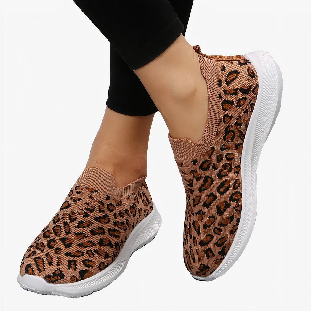 sur un sol gris, une paire de mocassins sport en maille à motif léopard et semelle épaisse blanche à enfiler portée les chevilles nues avec un legging noir