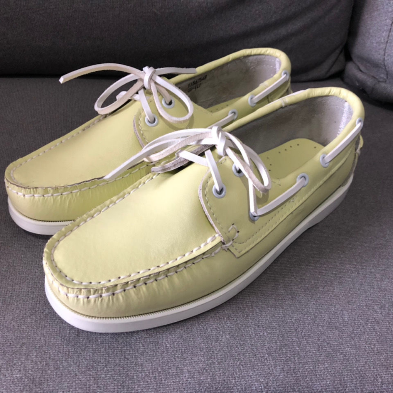 Paire de mocassins bateau jaune à lacets posé sur un sol gris