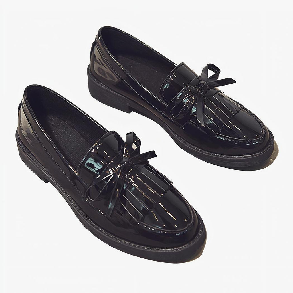 Paire de mocassins noirs vernis à frange posés au sur un sol gris