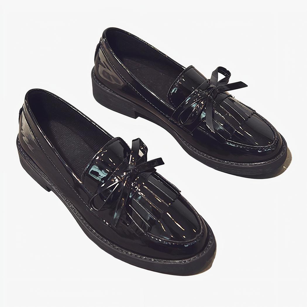 Paire de mocassins noirs vernis à frange posés au sur un sol gris