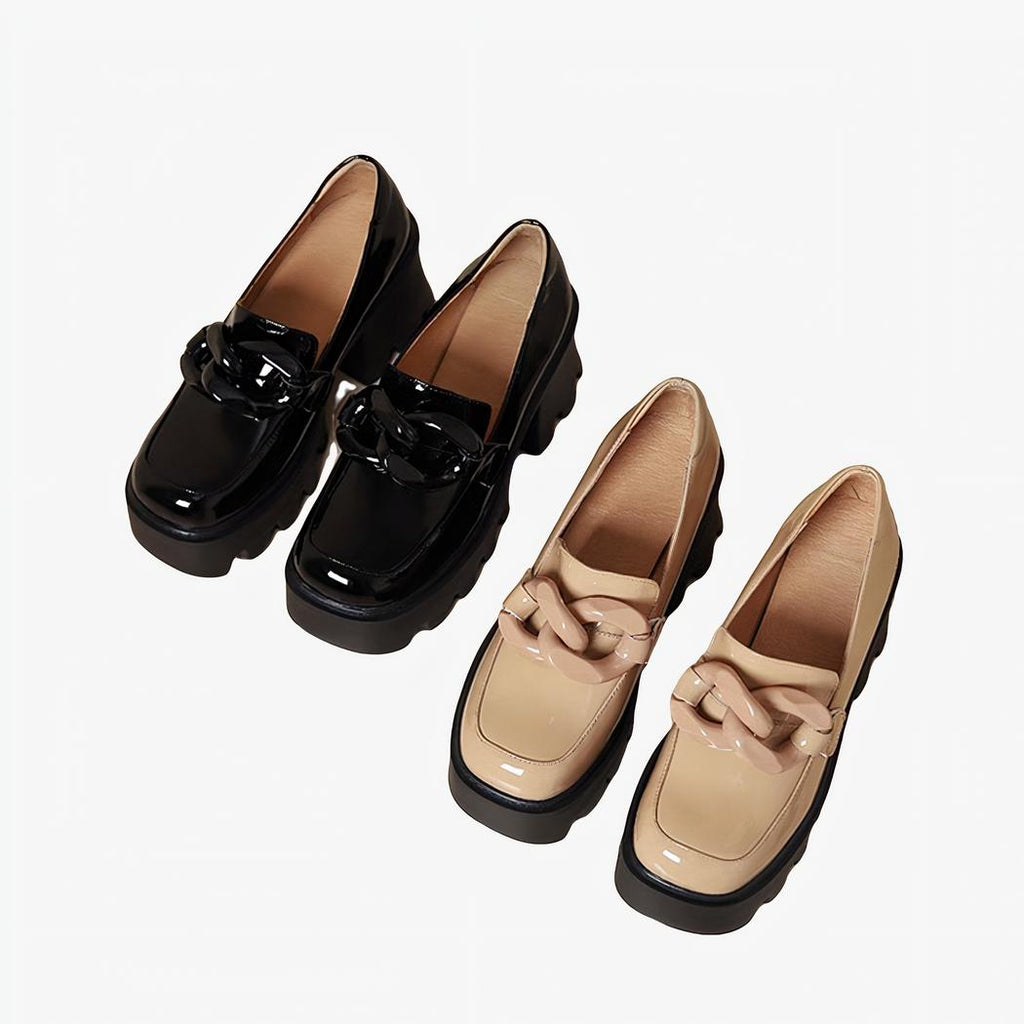 Deux paires de mocassins en cuir vernis, l'une noire l'autre beige, avec une boucle XXL en forme de signe de l'infini sur un fond beige clair.