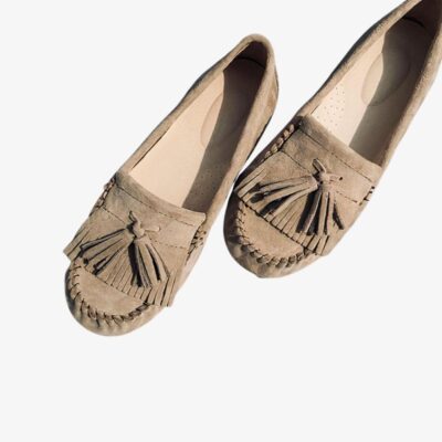 Mocassins en daim beige type mocassins indiens avec une frange et des glands, posés sur un fond clair