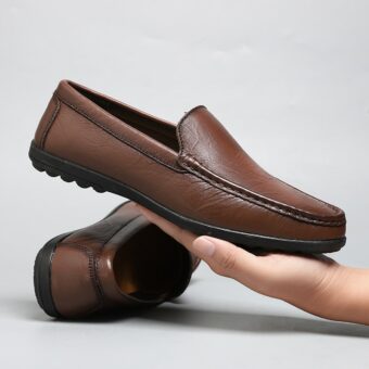 mocassin en cuir marron tenu dans la main d'un homme avec derrière l'autre paire de la chaussure