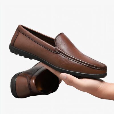 mocassin en cuir marron tenu dans la main d'un homme avec derrière l'autre paire de la chaussure