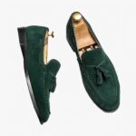 Paire de mocassins verts à pompons posés sur une surface à carreaux blancs