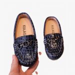 mocassin en faux cuir à motif croco pour bébé avec un anneau sur le dessus, ces chaussures sont présenter dans la main d'une femme