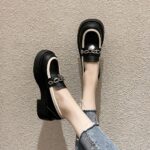 Photo d'une paire de mocassins à plateforme noire portée par une femme en jean sur un sol beige