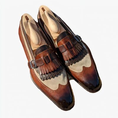 Une paire de mocassins semi-pointues en cuir lisse et en daim synthétique marron et beige avec franges bicolores et attache avec lanière et boucle sur le dessus.