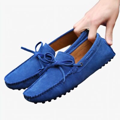 Paire de mocassins bleus tenus dans une main posée sur un banc en bois