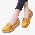 Photo d'une paire de mocassins compensée jaune portée par une femme en pantalon noir sur un sol gris