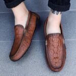 Photo d'une paire de mocassins marron portés par une femme avec un pantalon noir sur un sol gris