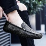 Photo d'un mocassin en cuir noir porté par une femme au pantalon noir dans une rue