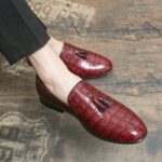 Pieds portant des mocassins rouges effet peau de crocodile et avec un gland sur le dessus de la chaussure